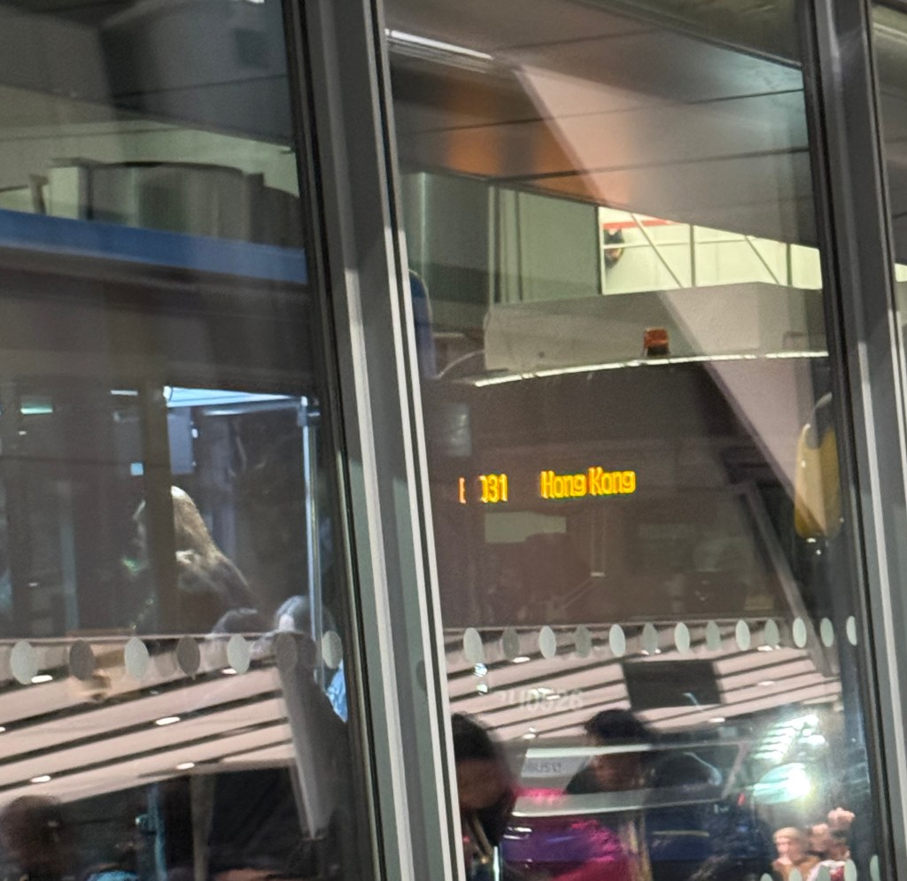 A bus stating its destination is Hong Kong, with lots of reflections inside the airport terminal